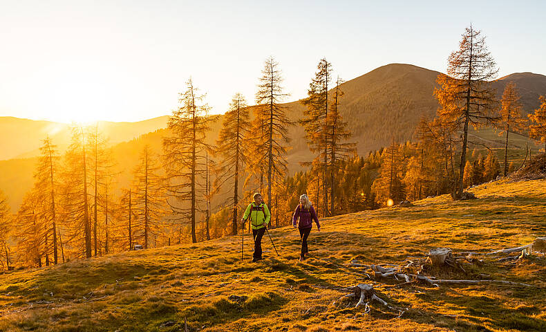 Wanderer bei Sonnenuntergang auf Etappe 7 des Nockberge Trail mit Ausblick Richtung Millstätter See im UNESCO Biosphärenpark.