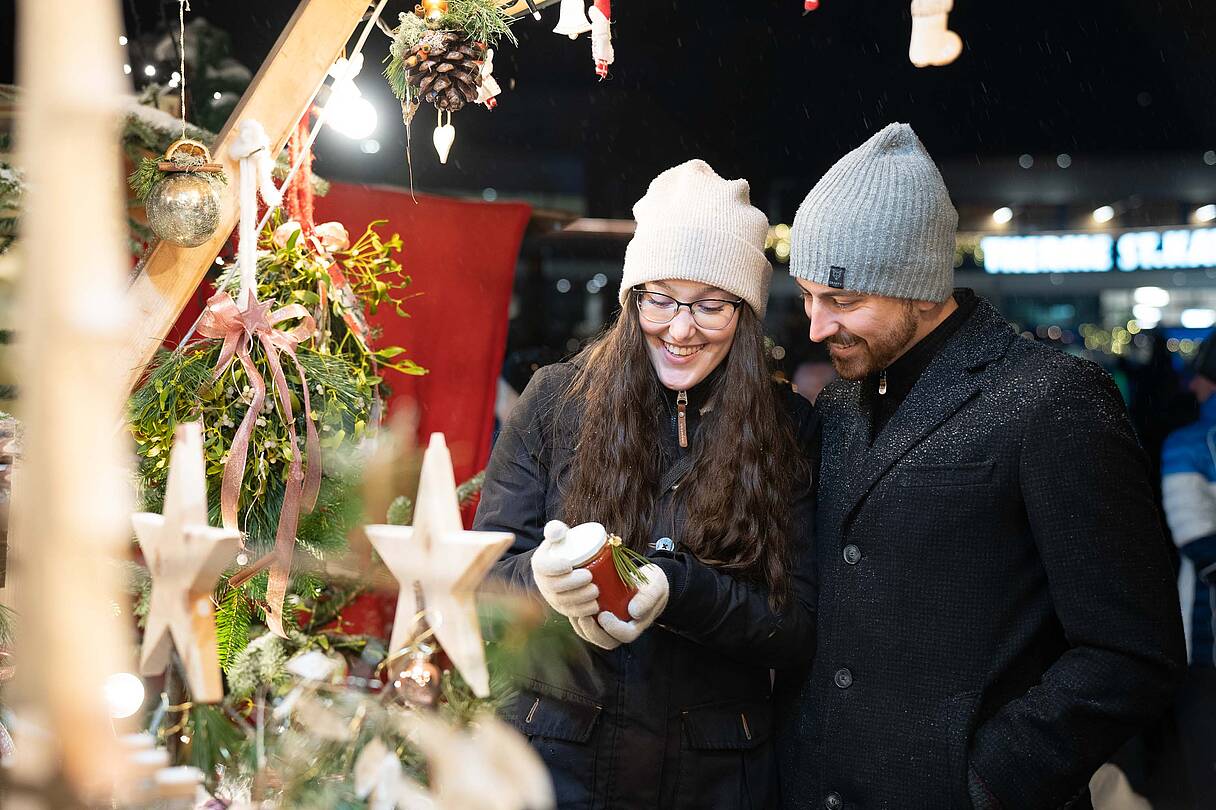 Paar sieht sich Stand am Kirchheimer Adventmarkt an und trinkt ein heißes Getränk