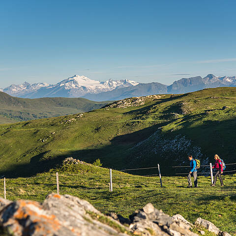 2 Personen wandern am Nockberge-Trail entlang mit einem atemberaubenden Bergpanorama
