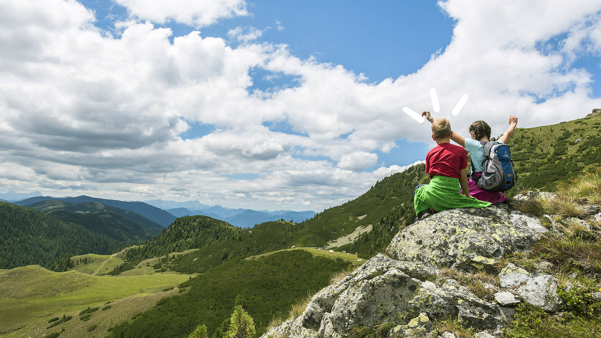2 Kinder sitzen auf einem Felsvorsprung und betrachten das Bergpanorama der Nockberge